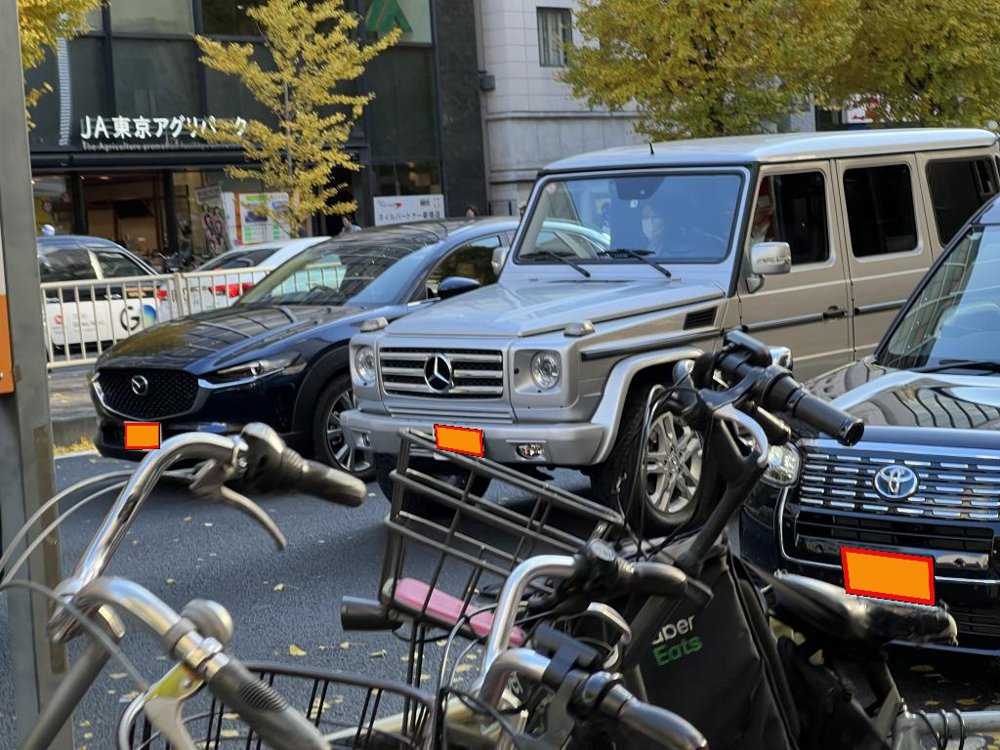 駐輪場越しに見える路上の車の写真